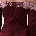 Close-up of the back of an off-the-shoulder burgundy dress with long sleeves, a lace-up corset-style back, and light pink floral lace trim across the shoulders.