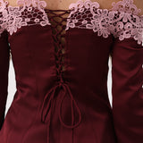 Close-up of the back of an off-the-shoulder burgundy dress with long sleeves, a lace-up corset-style back, and light pink floral lace trim across the shoulders.