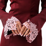 A woman modeling an off-the-shoulder burgundy satin mini dress with light pink floral lace trim around the cuffs and hem.