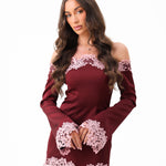A woman modeling a burgundy off-the-shoulder long-sleeve mini dress with light pink floral lace trim at the neckline, cuffs, and hem, set against a plain white background.