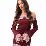 A woman modeling a burgundy off-the-shoulder long-sleeve mini dress with light pink floral lace trim at the neckline, cuffs, and hem, set against a plain white background.