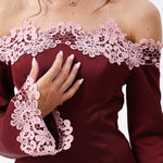 A woman modeling an off-the-shoulder burgundy satin mini dress with light pink floral lace trim and loose sleeves.
