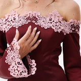 A woman modeling an off-the-shoulder burgundy satin mini dress with light pink floral lace trim and loose sleeves.