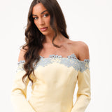 A woman modeling an off-the-shoulder pale yellow dress with light blue lace trim across the neckline, set against a plain white background.