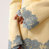 Close-up of a pale yellow dress with long flared sleeves and dusty blue lace trim at the cuffs and hem, shown on a model.