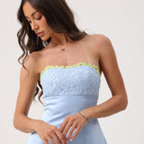 A woman wearing a strapless light blue dress with a floral lace bodice and a thin lime green trim along the neckline, photographed against a plain light background.