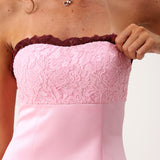 A woman modeling a light pink strapless mini dress with dark burgundy ruffle trim at the neckline and hem.