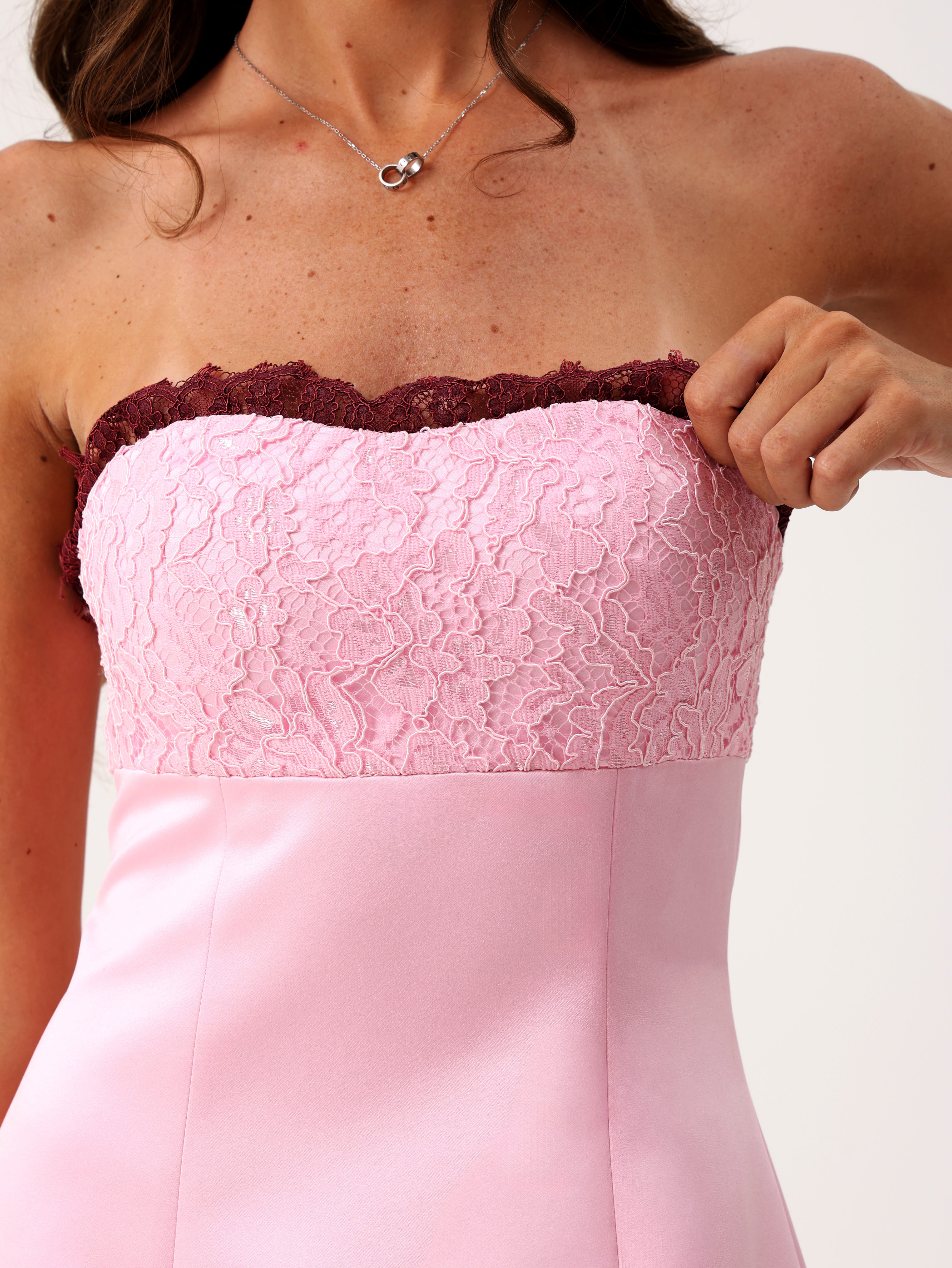 A woman modeling a light pink strapless mini dress with dark burgundy ruffle trim at the neckline and hem.