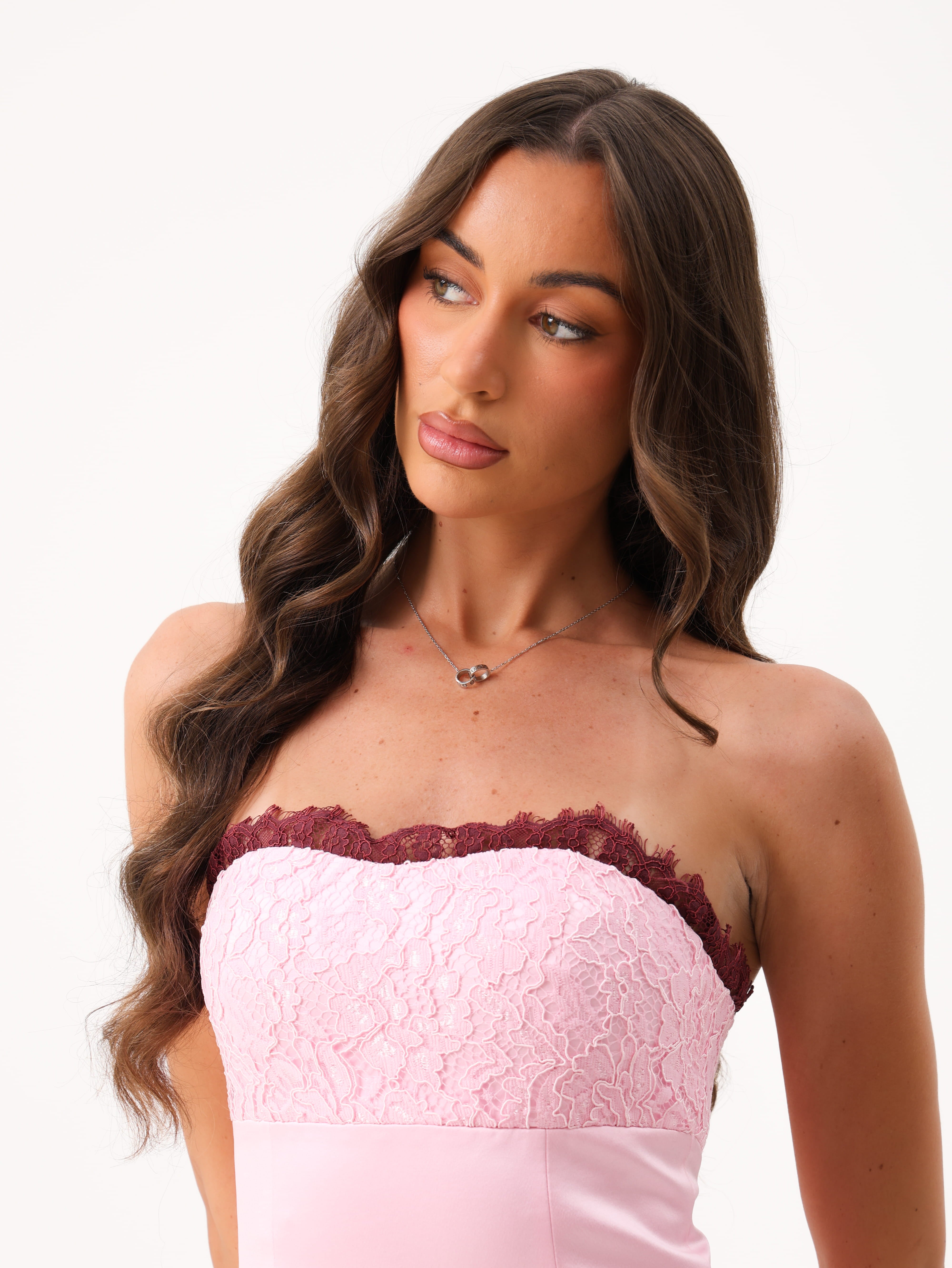 A woman modeling a light pink strapless tube top with a darker burgundy lace trim against a plain white background.
